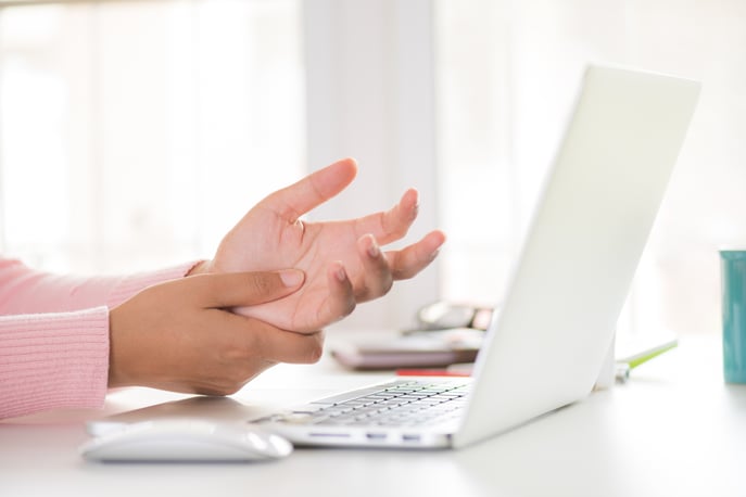 Woman rubbing her palm from discomfort while using a laptop