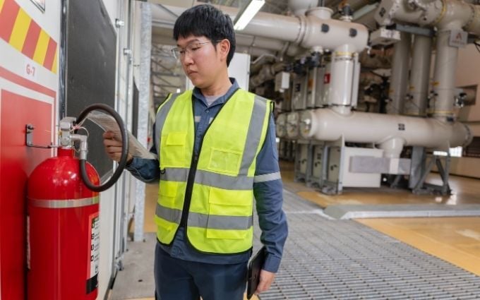 Electrical engineer checking fire extinguisher record inside power substation, ensuring workplace safety compliance, emergency readiness, and preventive inspection standards.