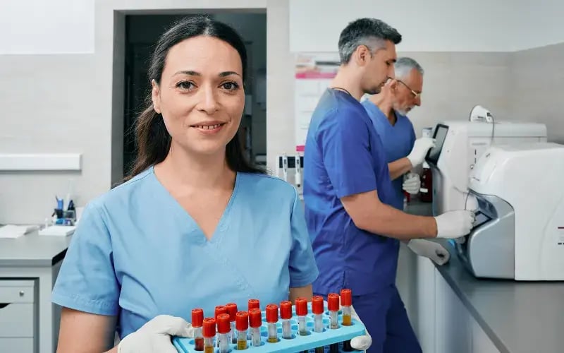 Diagnostic laboratory scientist holding test tube rack with samples near laboratory workers who conducts research on lab machines