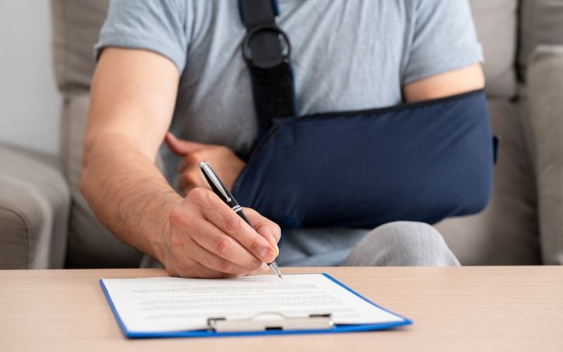 Man with arm in sling signs paperwork