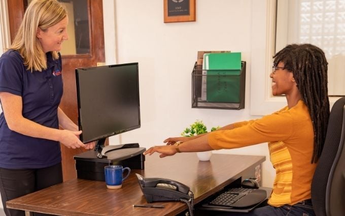 Woman sitting at desk with her arms outstretched to optimize her monitor placement